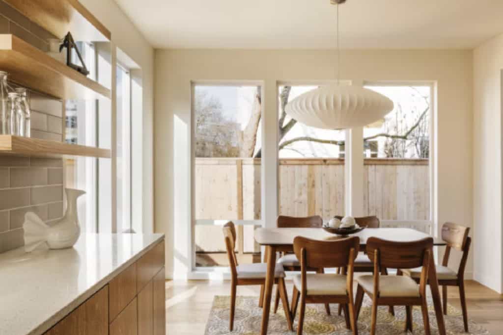 Bright mid-century modern dining area featuring large windows allowing natural light and minimalist open shelving in a neutral-toned kitchen