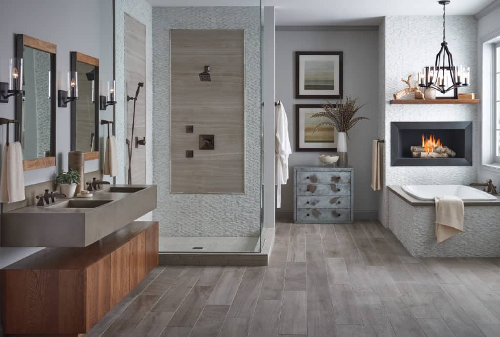 Modern bathroom with dual vanity, wood cabinets, tile shower, tub with fireplace, and gray tones
