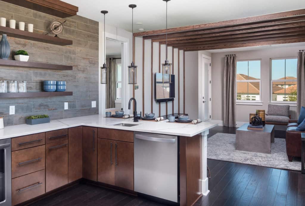 Modern kitchen design services from Coburn’s featuring rich wood cabinets, white countertop, stainless steel appliances, wooden shelves, and pendant lights hanging over the counter