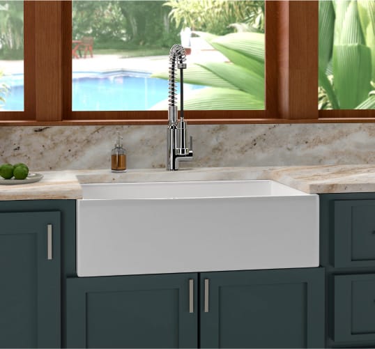 A porcelain basin kitchen sink surrounded by granite countertops and deep teal cabinets. Get more kitchen upgrade ideas at a Coburn's Kitchen & Bath Showroom.