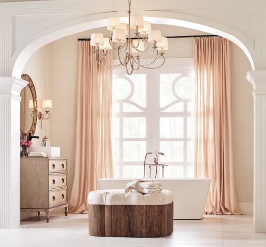 A soft pastel bathroom with blush curtains, freestanding soaker tub and graceful chandelier that's perfect for your list of bathroom renovation ideas.