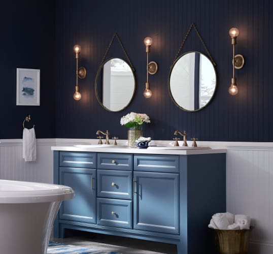 A dark and moody bathroom with a blue vanity sink and ambient sconce lighting. Get more bathroom design ideas at Coburn's Kitchen & Bath Showroom