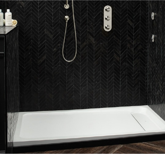 a dark alcove shower with a white base for a pop of color. The black tiles and dark floor paneling offer the perfect bathroom inspiration to fans of the bold