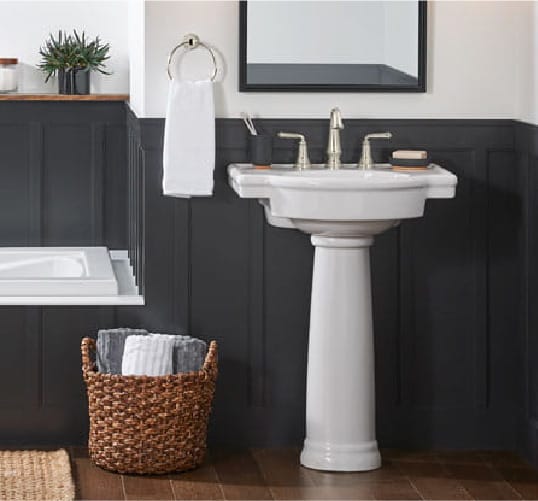 a pedestal bathroom sink surrounded by dark blue paneling and white walls all tied together with dark wood accents. Discover more bathroom design ideas at Coburn's Kitchen & Bath Showroom